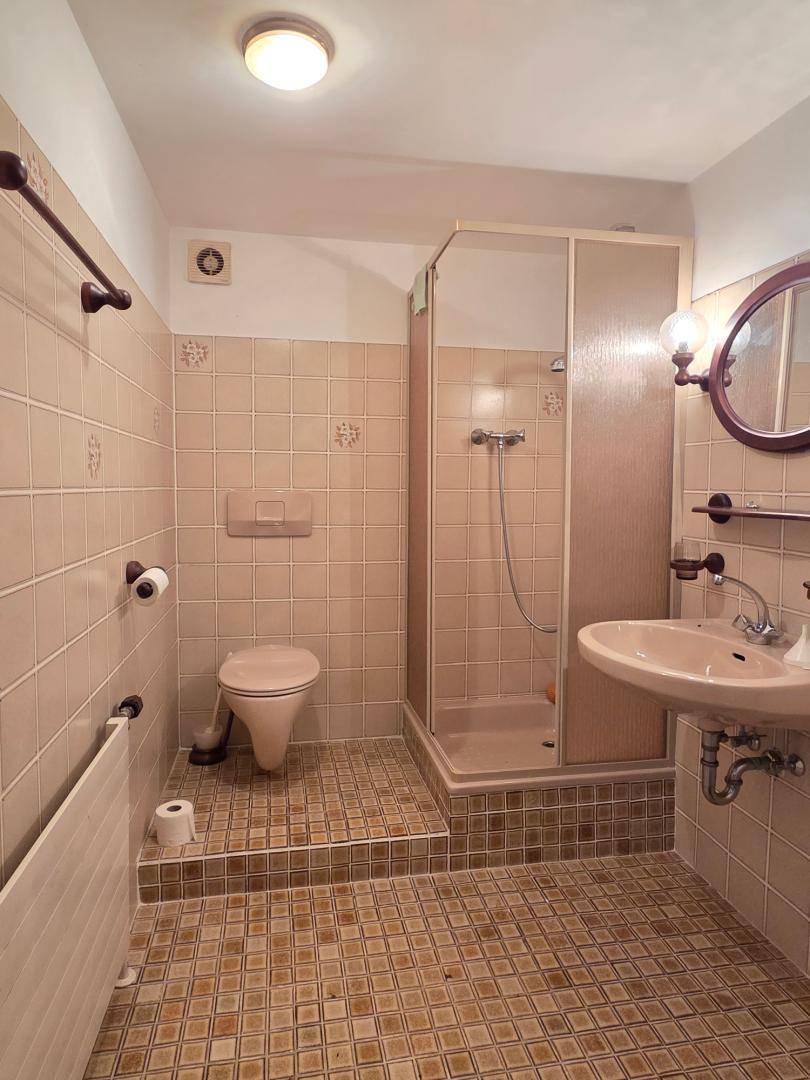 Badezimmer mit Dusche, WC und beigefarbenen Fliesen im traditionellen Stil.