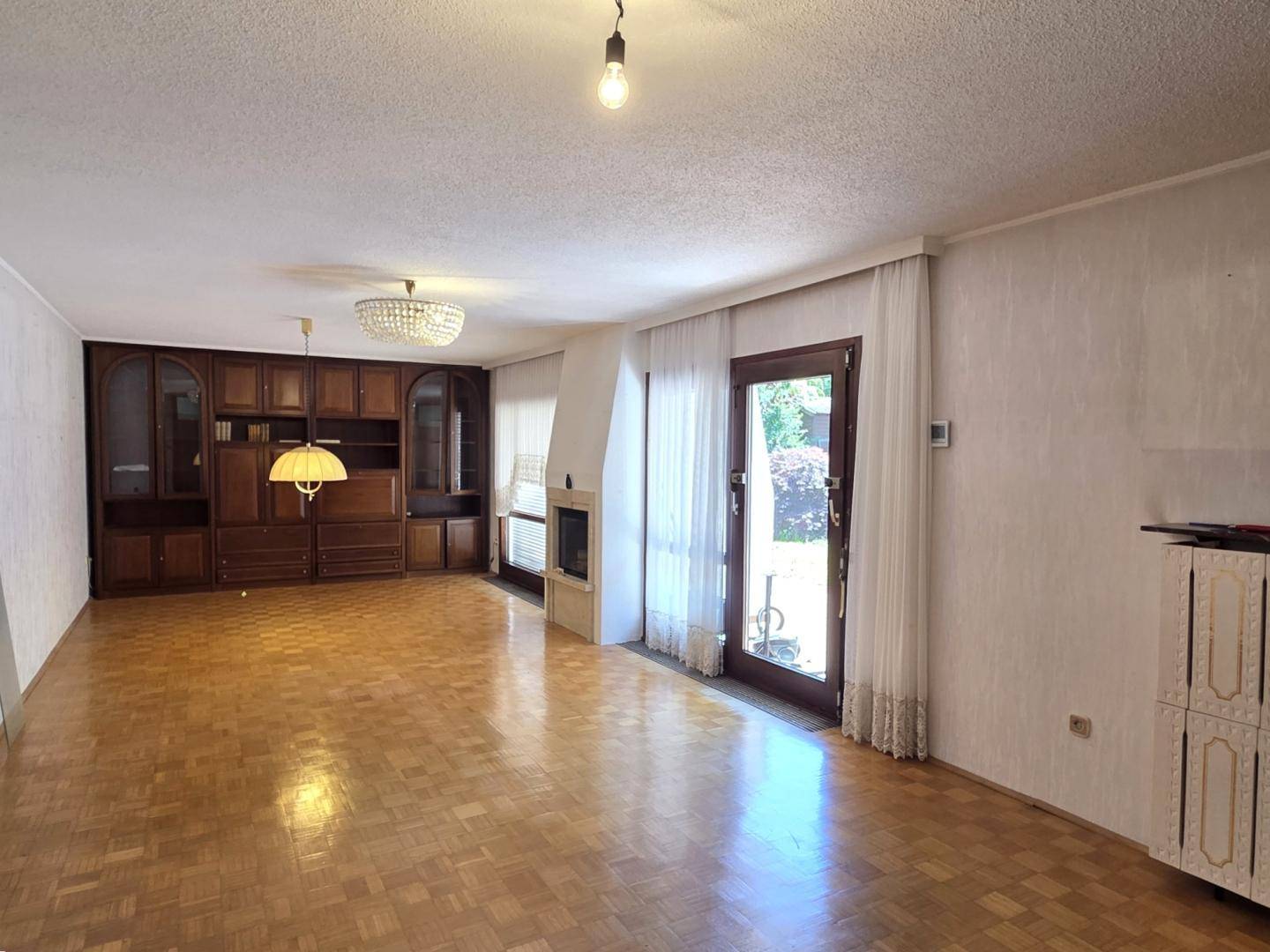 Helles Wohnzimmer mit Parkettboden, Einbauschränken und Blick in den Garten.