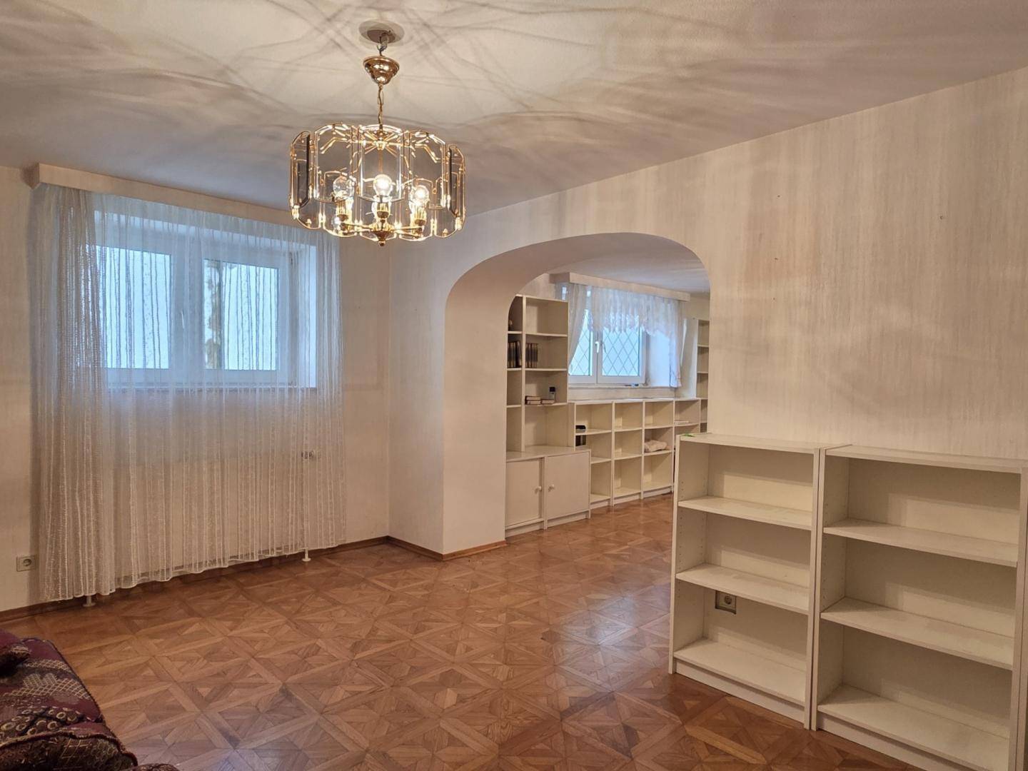 Heller Wohnbereich mit Parkettboden, großen Fenstern und integrierten Bücherregalen.