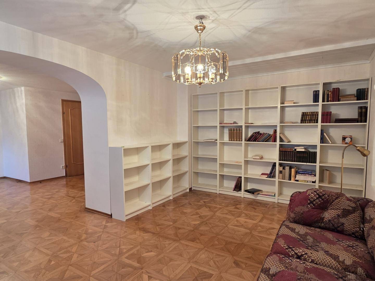 Wohnzimmer mit Parkettboden, Bücherregalen und einem Durchgang zu einem weiteren Bereich.