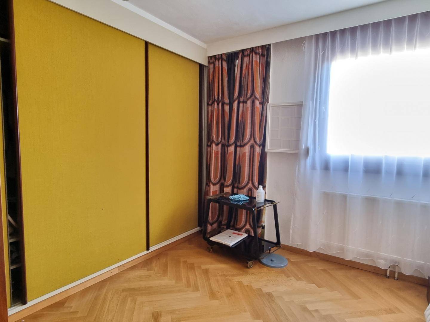 Schlafzimmer mit Parkettboden, gelben Schiebetüren und einem Fenster mit Vorhang.