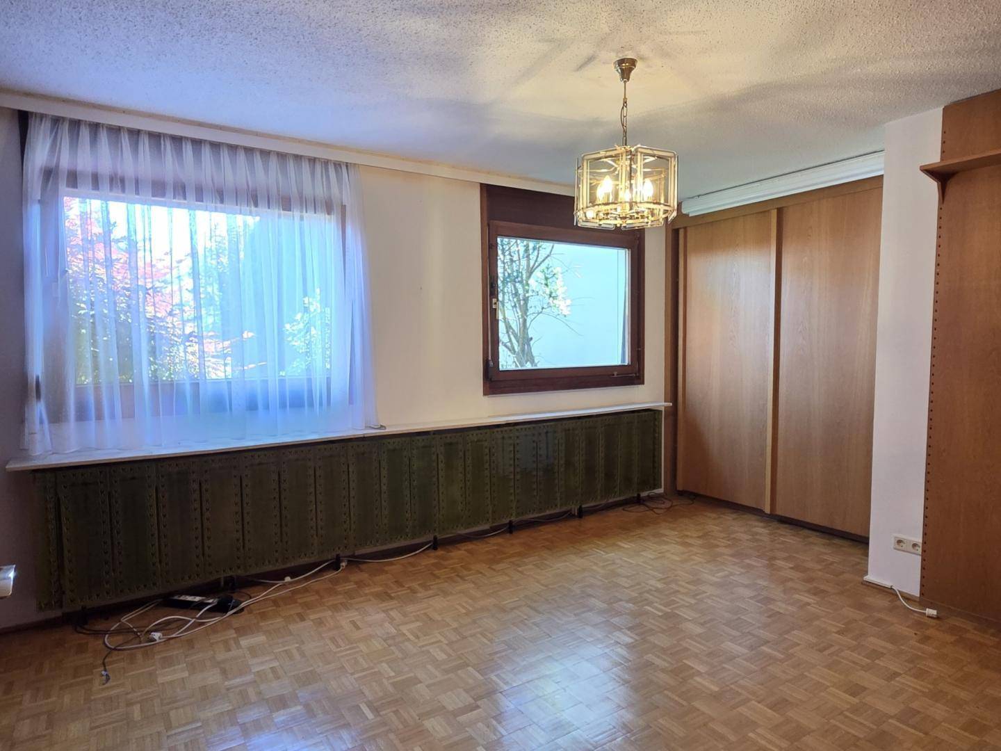 Schlafzimmer mit Parkettboden, großen Fenstern und integrierten Holzschränken.