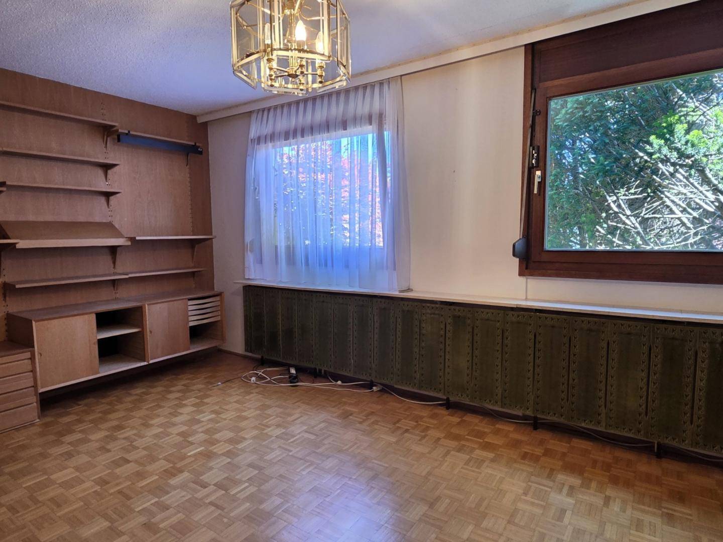 Schlafzimmer mit Parkettboden, Einbauregalen und Blick ins Grüne durch das Fenster.