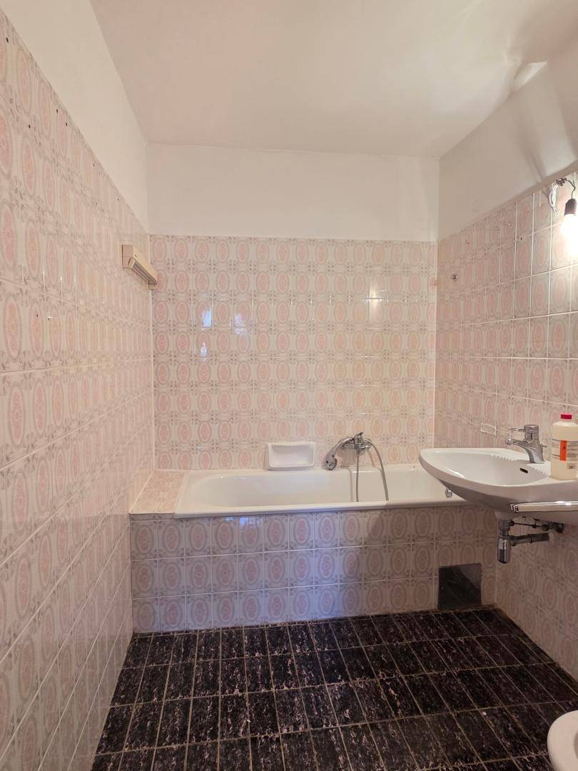 Badezimmer mit Badewanne und rosa gemusterten Fliesen im Stil der 80er Jahre.