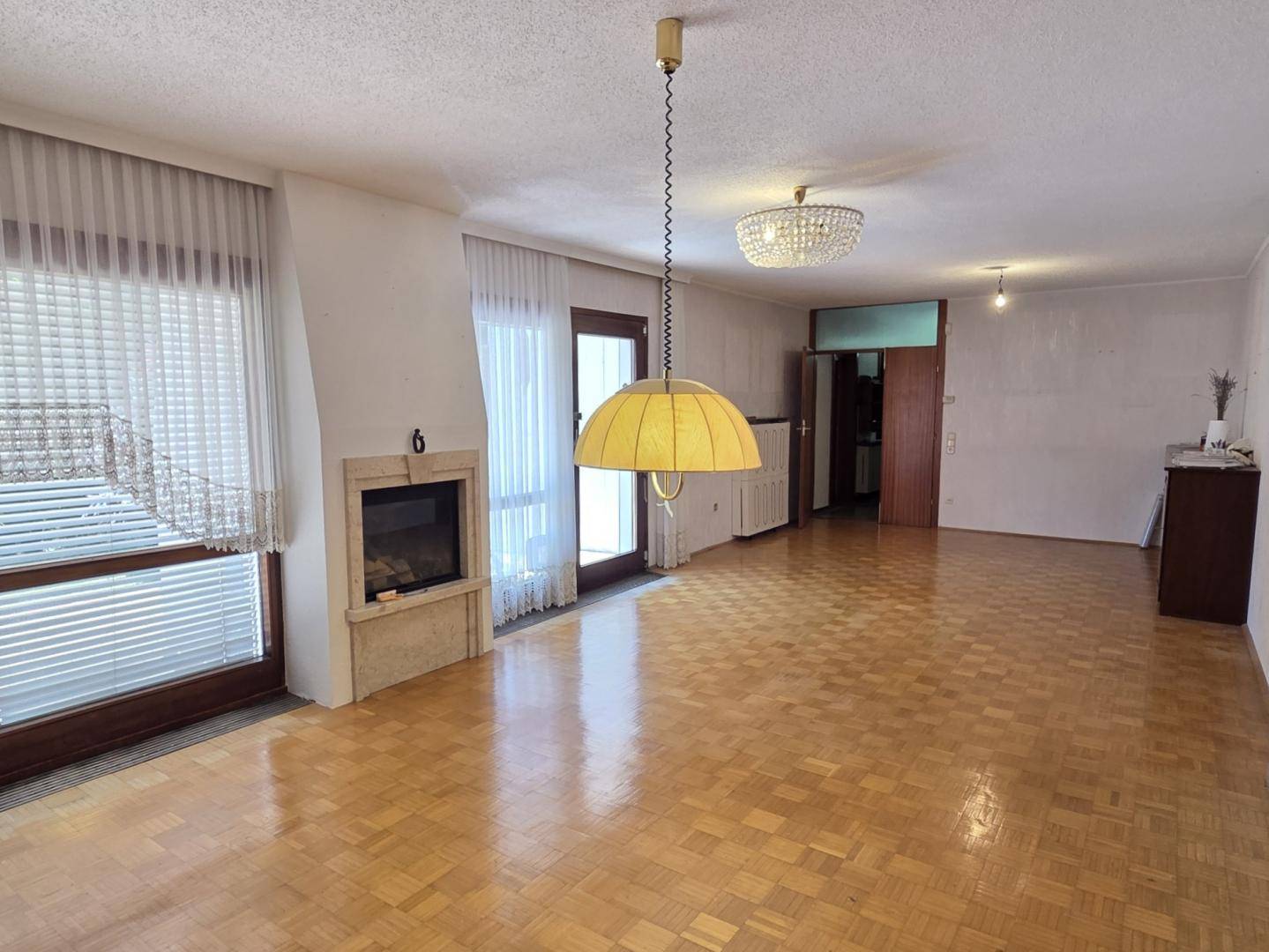 Geräumiges Wohnzimmer mit Fischgrätparkett, Kamin und Zugang zur Terrasse.