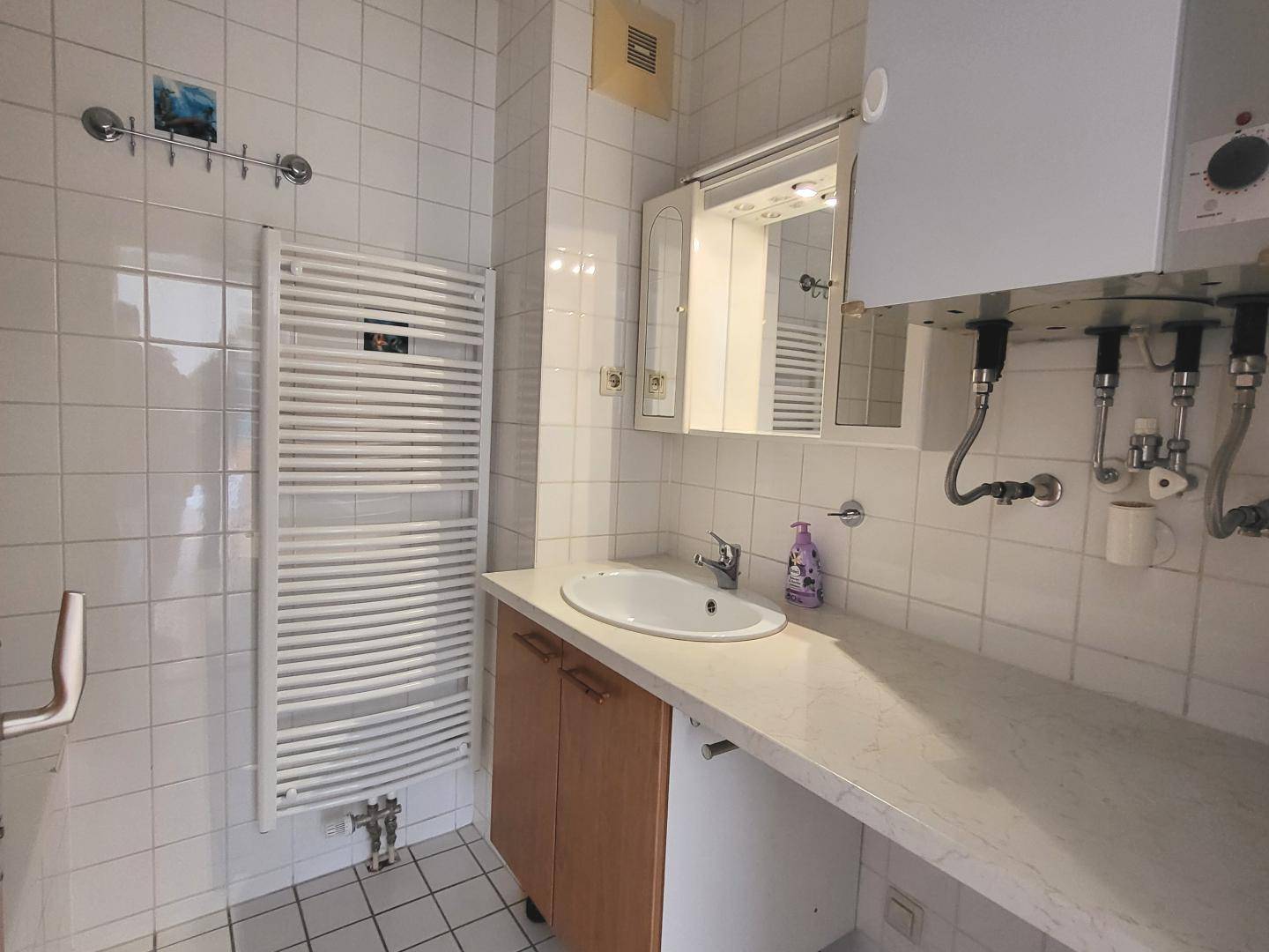 Gefliestes Badezimmer mit Waschbecken, Spiegelschrank und Handtuchheizkörper.