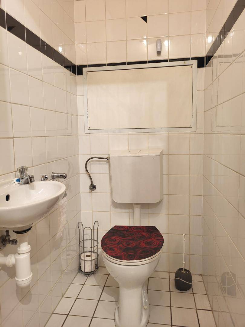 Kleines Gäste-WC mit Fliesen, Waschbecken und WC mit gemustertem Sitz.