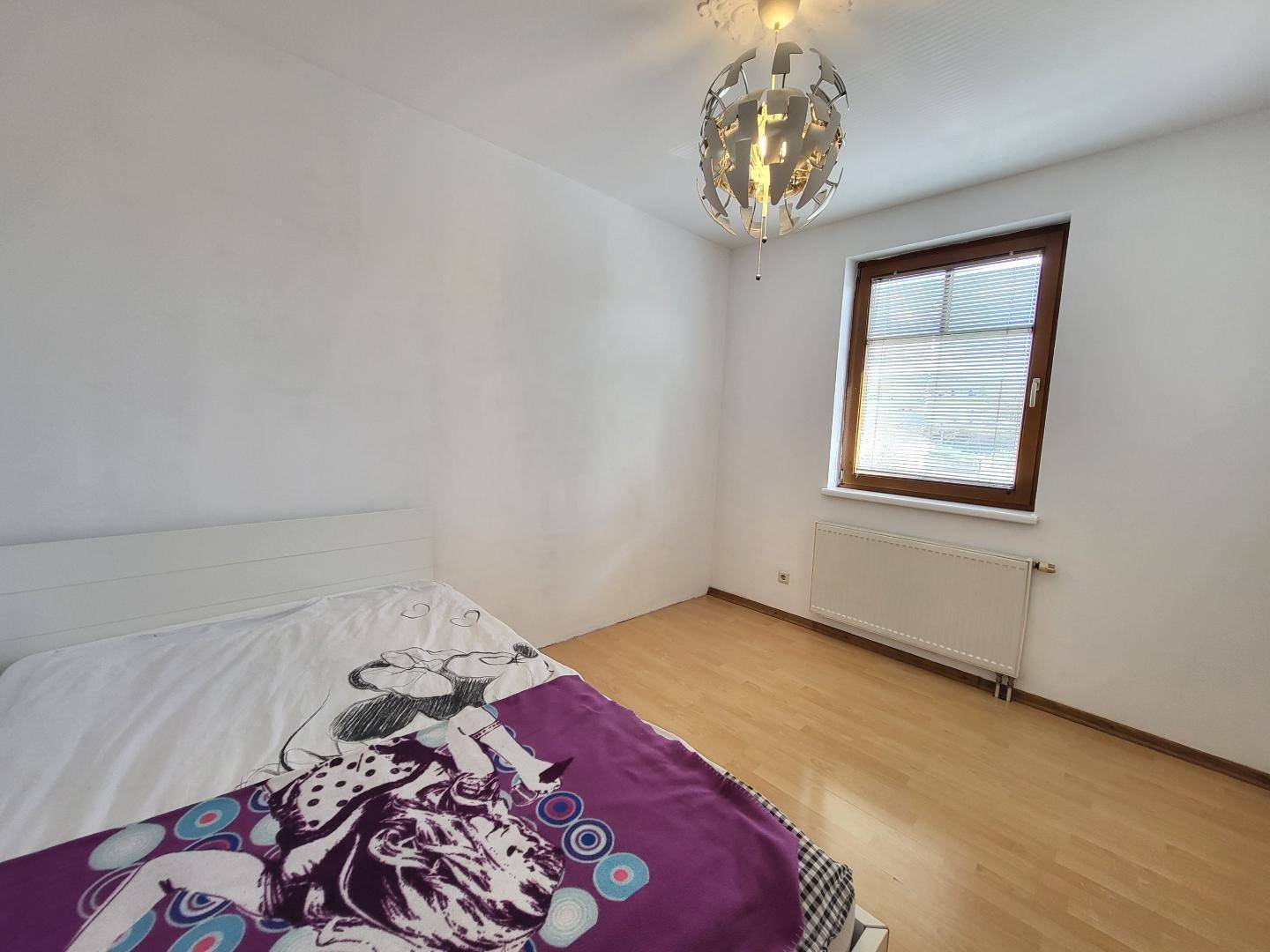 Schlafzimmer mit hellem Laminatboden, Fenster und moderner Deckenleuchte.