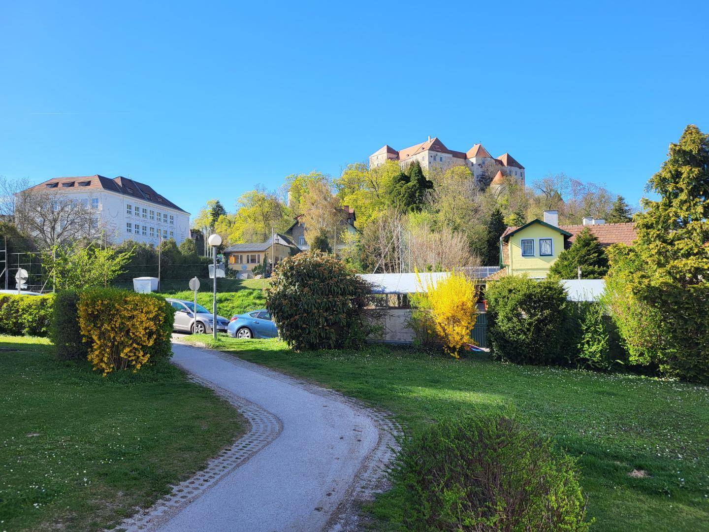 Malerische Umgebung mit historischer Burg auf einem Hügel und viel Grün.