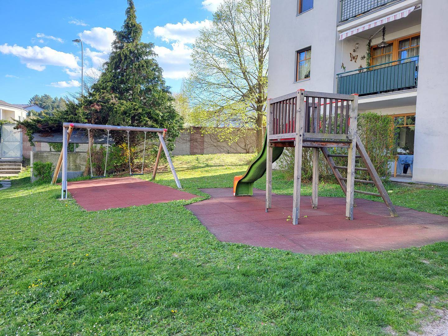 Gemeinschaftlicher Spielplatz mit Schaukel und Rutsche auf einer Grünfläche.