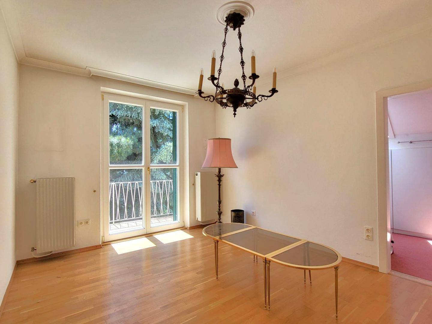 Heller Wohnraum mit Parkettboden, Fenster, Heizkörper und Zugang zu einem französischen Balkon.