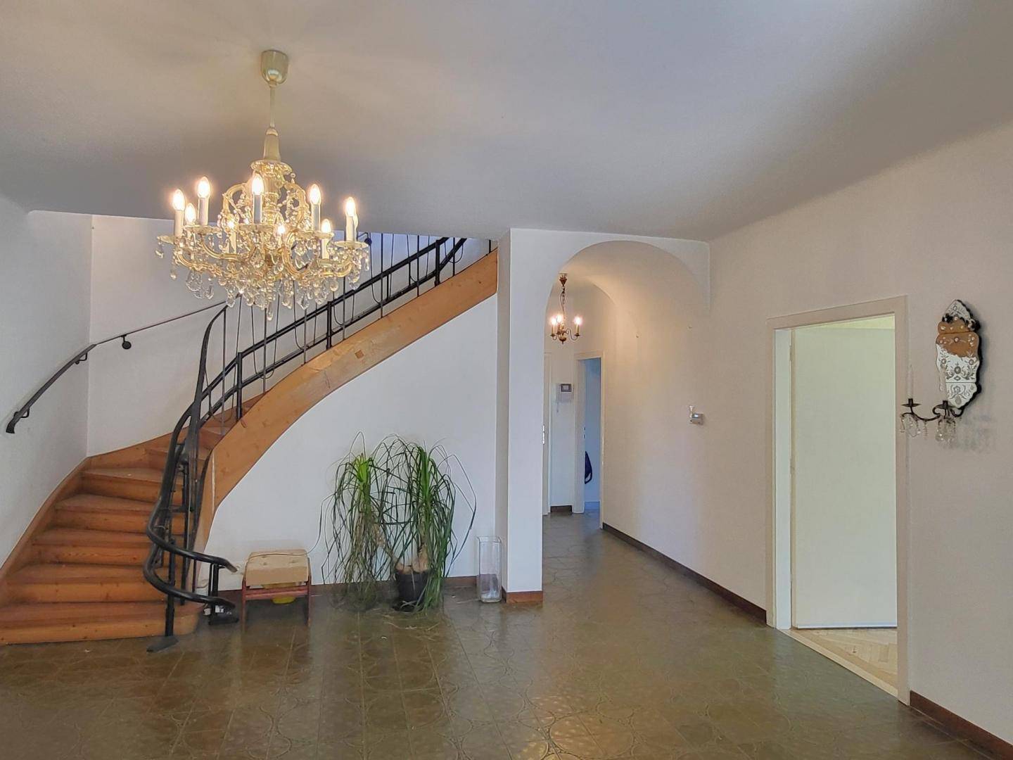 Geräumiger Eingangsbereich mit eleganter geschwungener Holztreppe und einem prunkvollen Kronleuchter.