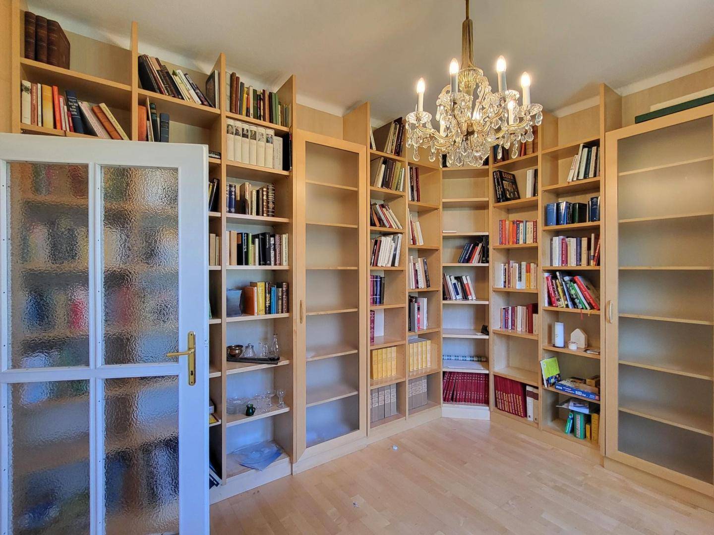 Helles Arbeitszimmer mit raumhohen, maßgefertigten Holzregalen und einem eleganten Kronleuchter.