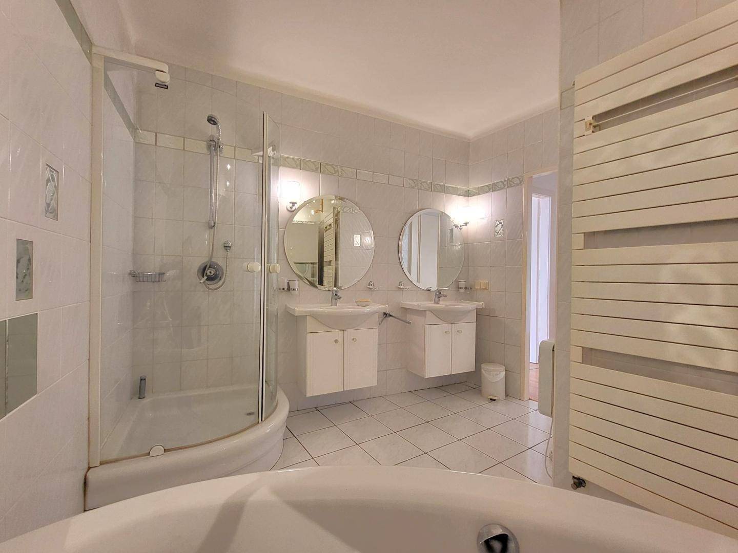 Helles Badezimmer mit weißen Fliesen, Doppelwaschbecken, Duschkabine und Badewanne.