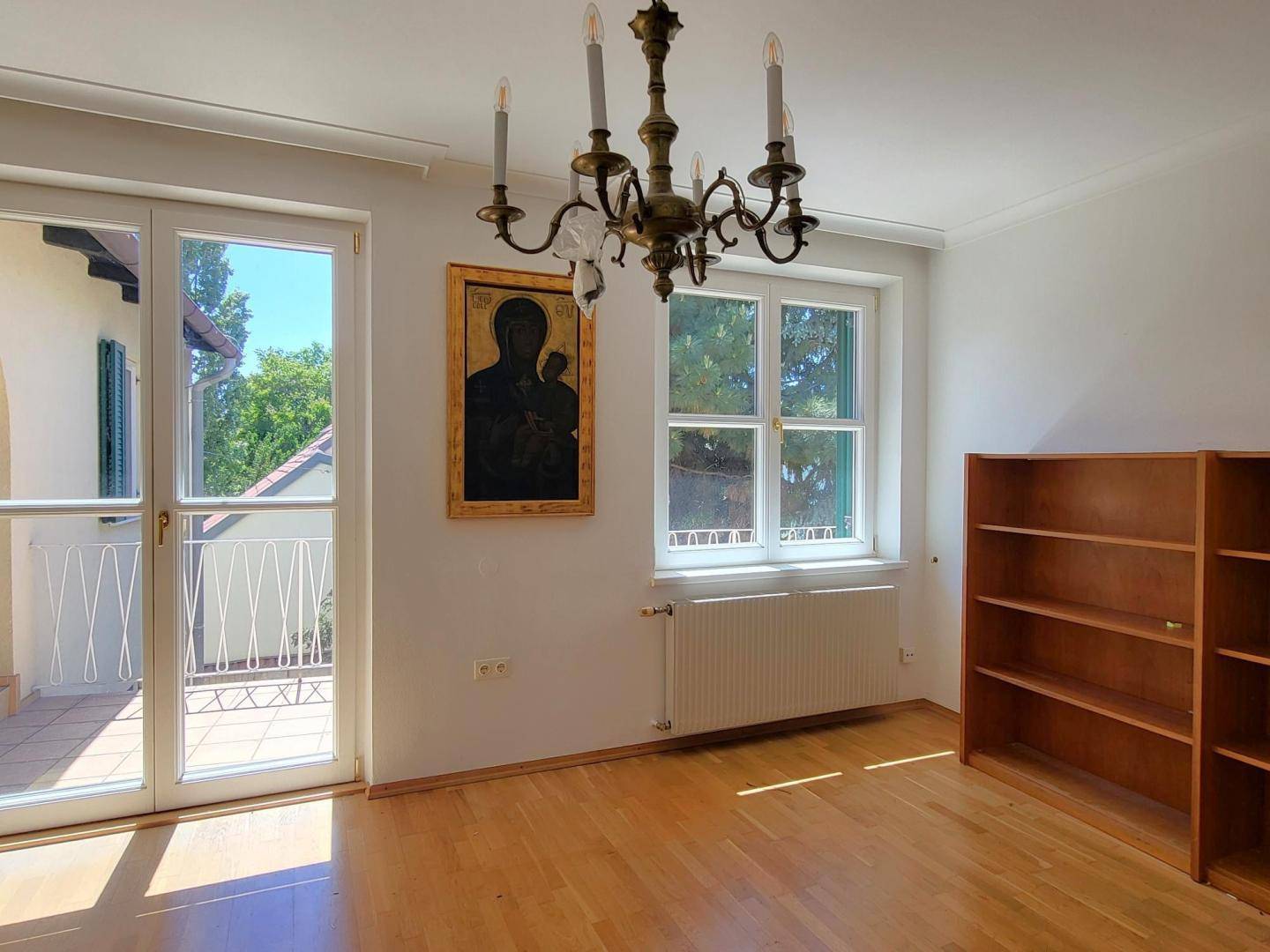 Heller Raum mit Parkettboden, großem Fenster und direktem Zugang zu einem Balkon.