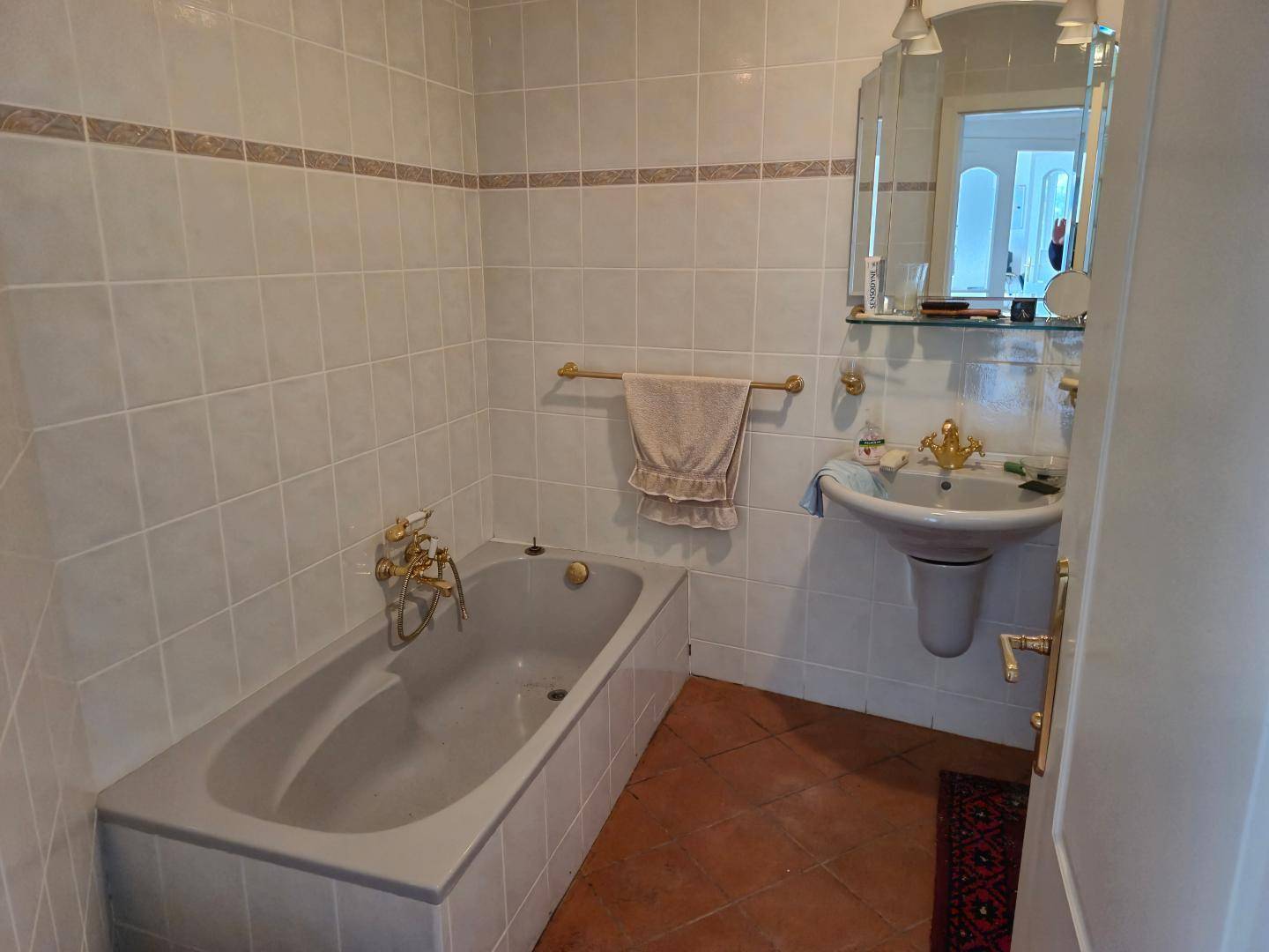 Badezimmer mit Badewanne, Waschbecken, Spiegel und weißen Fliesen, ausgestattet mit goldenen Armaturen.