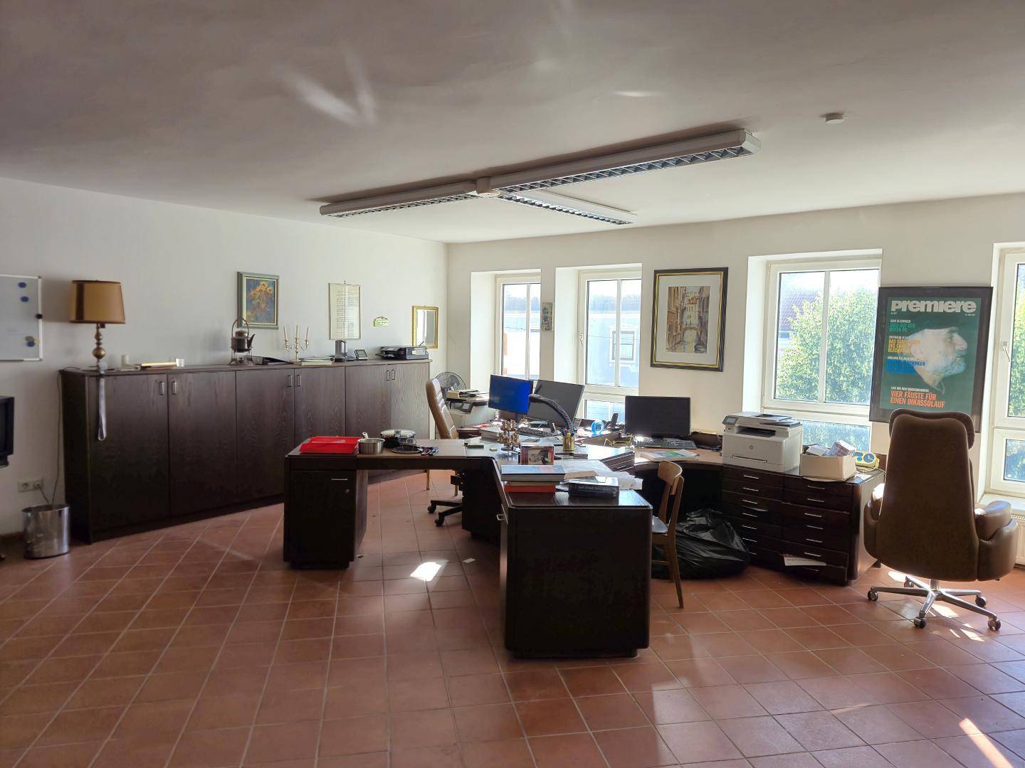 Möbliertes Büro mit mehreren Arbeitsplätzen, dunklen Schränken und Terrakotta-Fliesenboden.