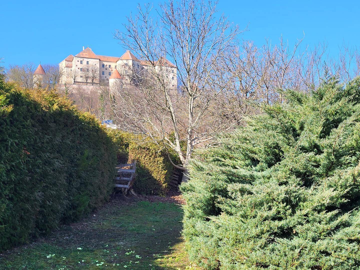 Gartenweg zwischen Hecken mit Blick auf die imposante Burg im Hintergrund.