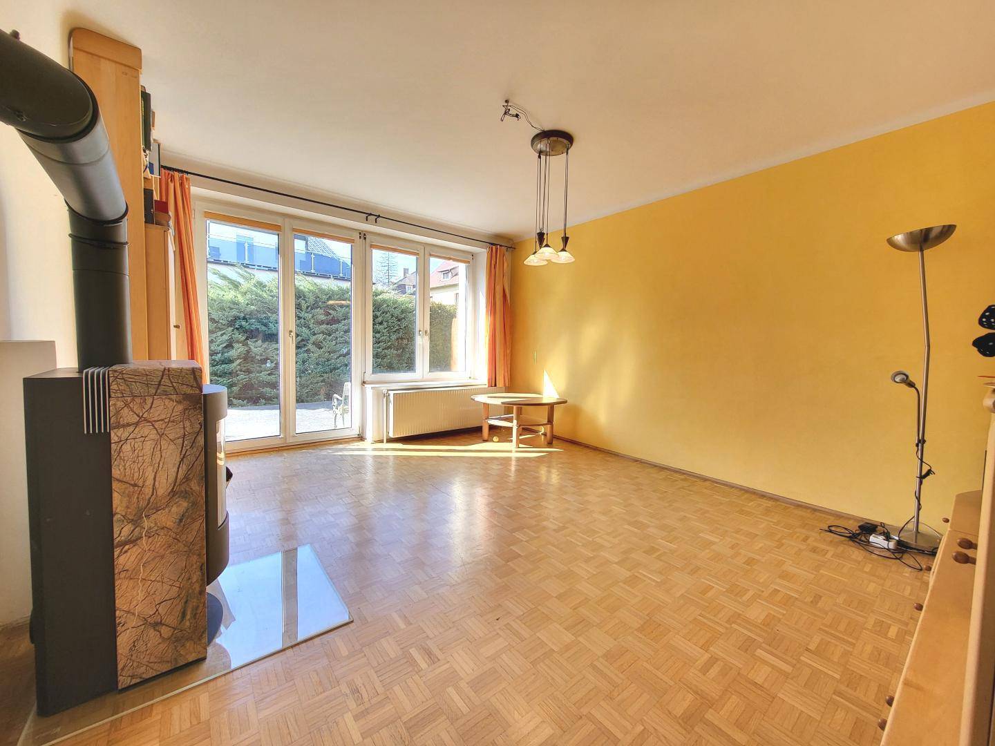 Helles Wohnzimmer mit Parkettboden, Kaminofen und Zugang zur Terrasse.