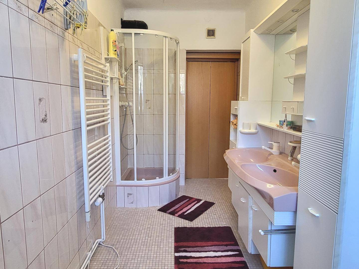 Badezimmer mit Duschkabine, Waschbecken und beheiztem Handtuchhalter.