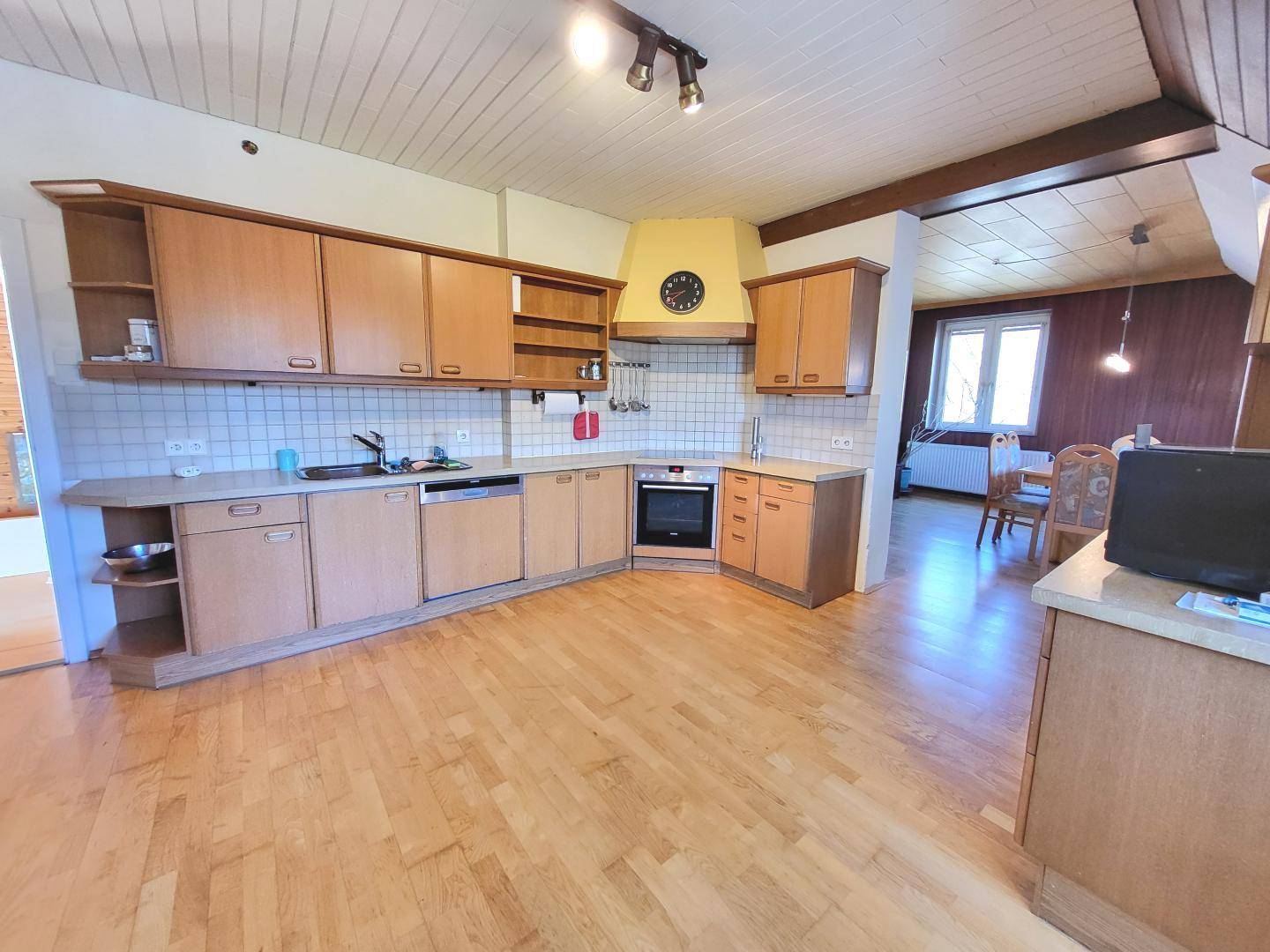 Geräumige Küche mit Holzschränken, Einbaugeräten und Essbereich im Hintergrund.