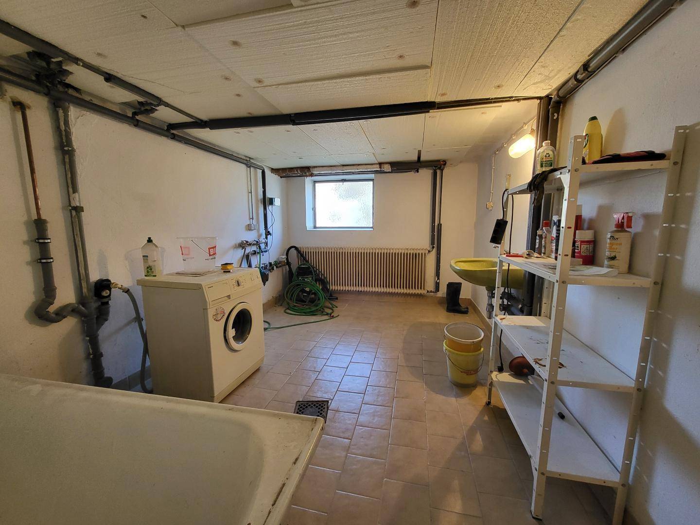 Waschküche im Keller mit Waschmaschine, Spülbecken und Fenster.