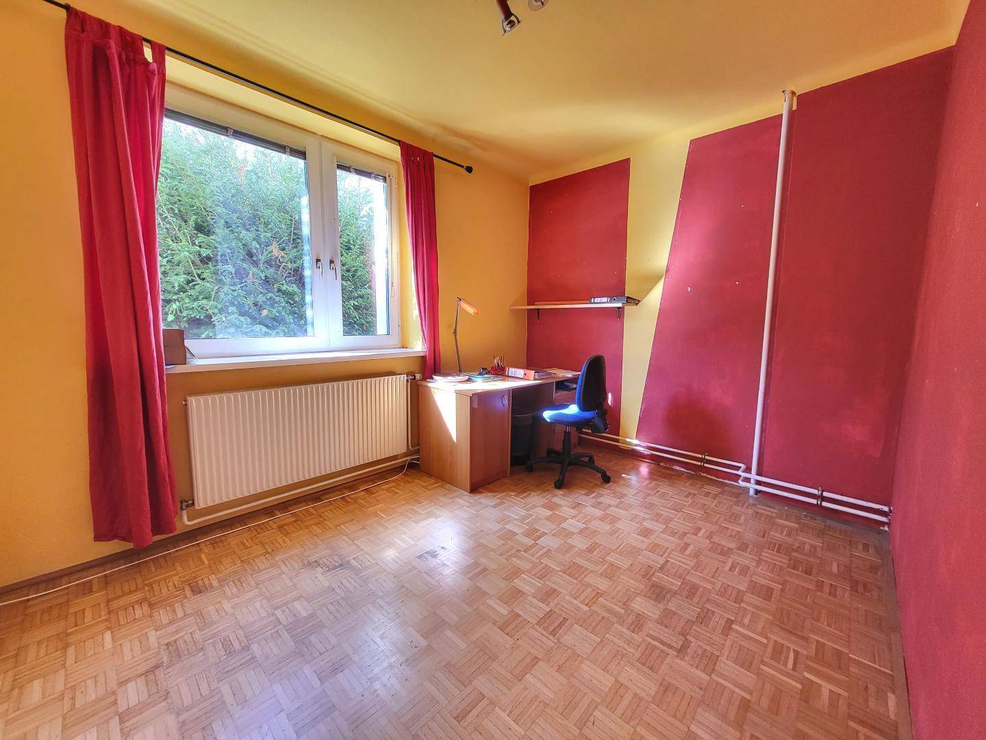 Farbenfrohes Zimmer mit Parkettboden, Schreibtisch und Blick ins Grüne.