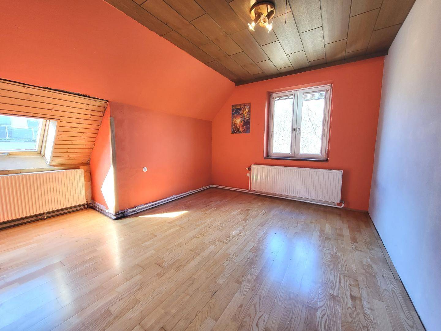 Helles Dachgeschosszimmer mit Holzboden, orangefarbenen Wänden und Dachfenster.