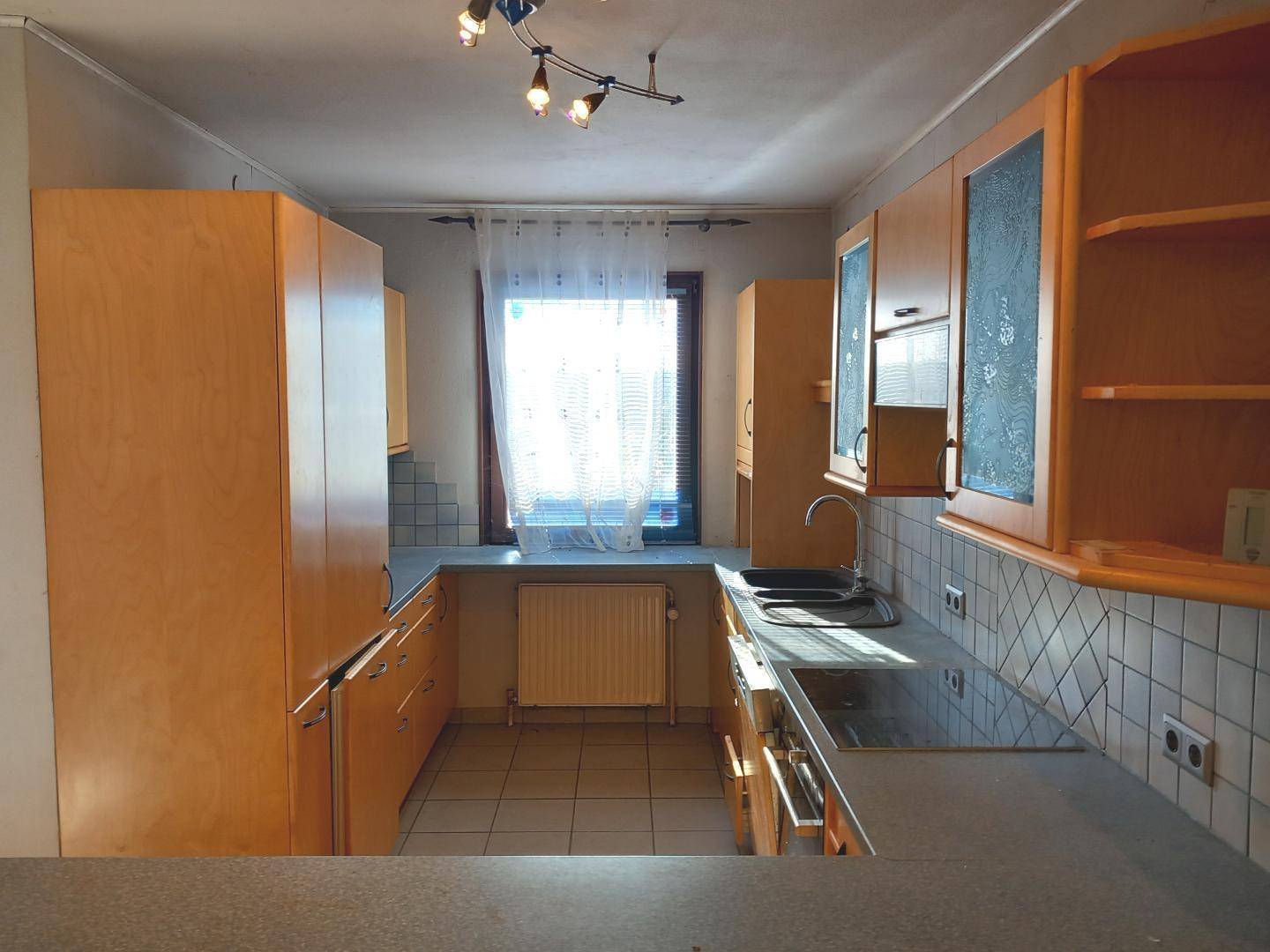 Ältere Küche mit Holzschränken, Fliesenboden und Fenster, bereit zur Renovierung.