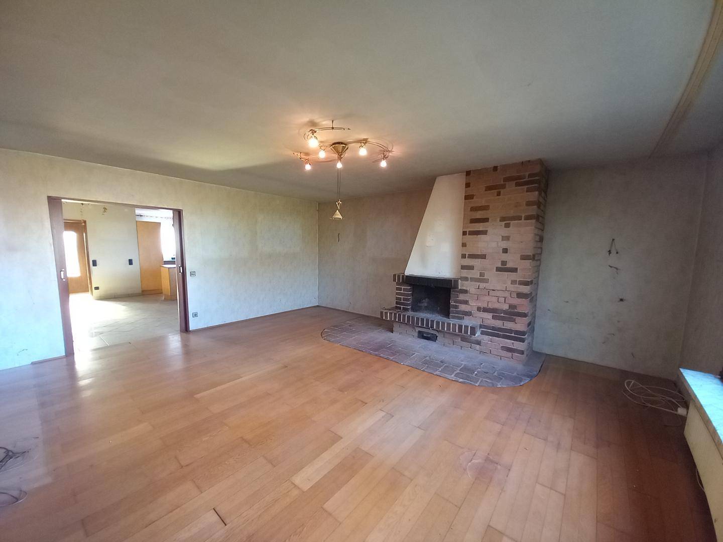 Helles Wohnzimmer mit Kamin und Holzboden, bietet Zugang zu einem weiteren Raum.