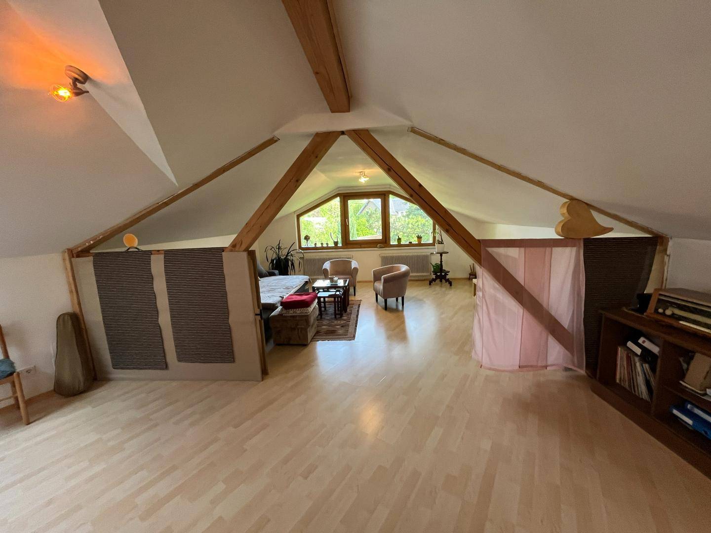 Heller Dachgeschossbereich mit gemütlicher Sitzecke und sichtbaren Holzbalken.