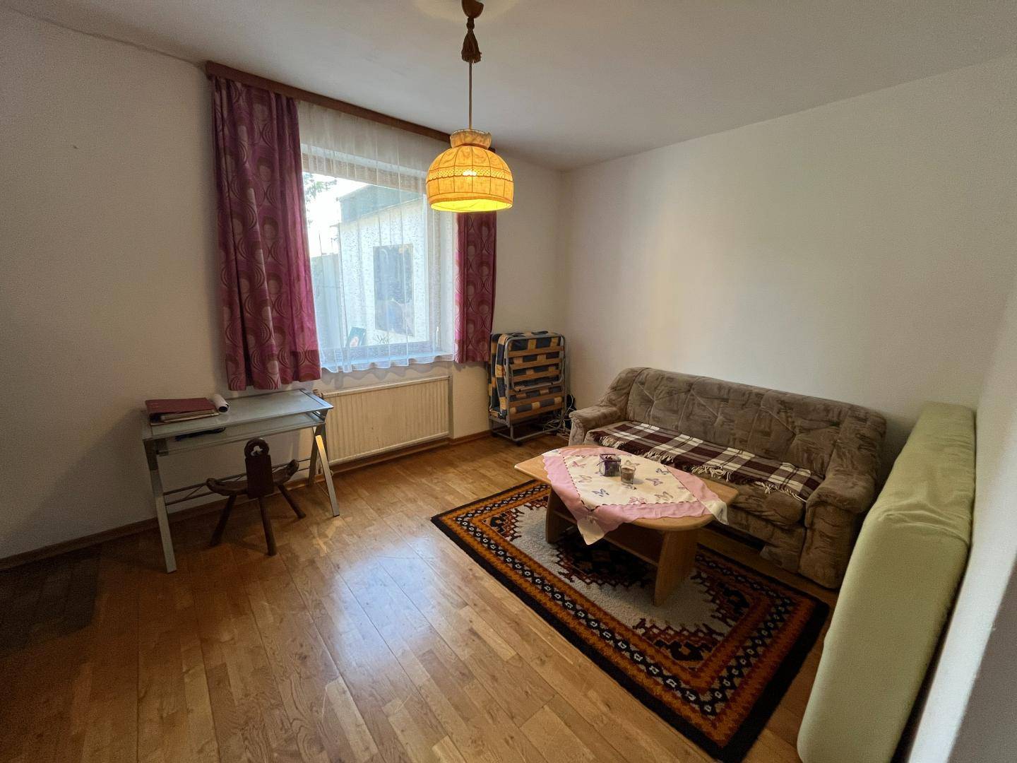 Helles Schlafzimmer mit Holzfußboden, einfacher Einrichtung und Fensterblick.
