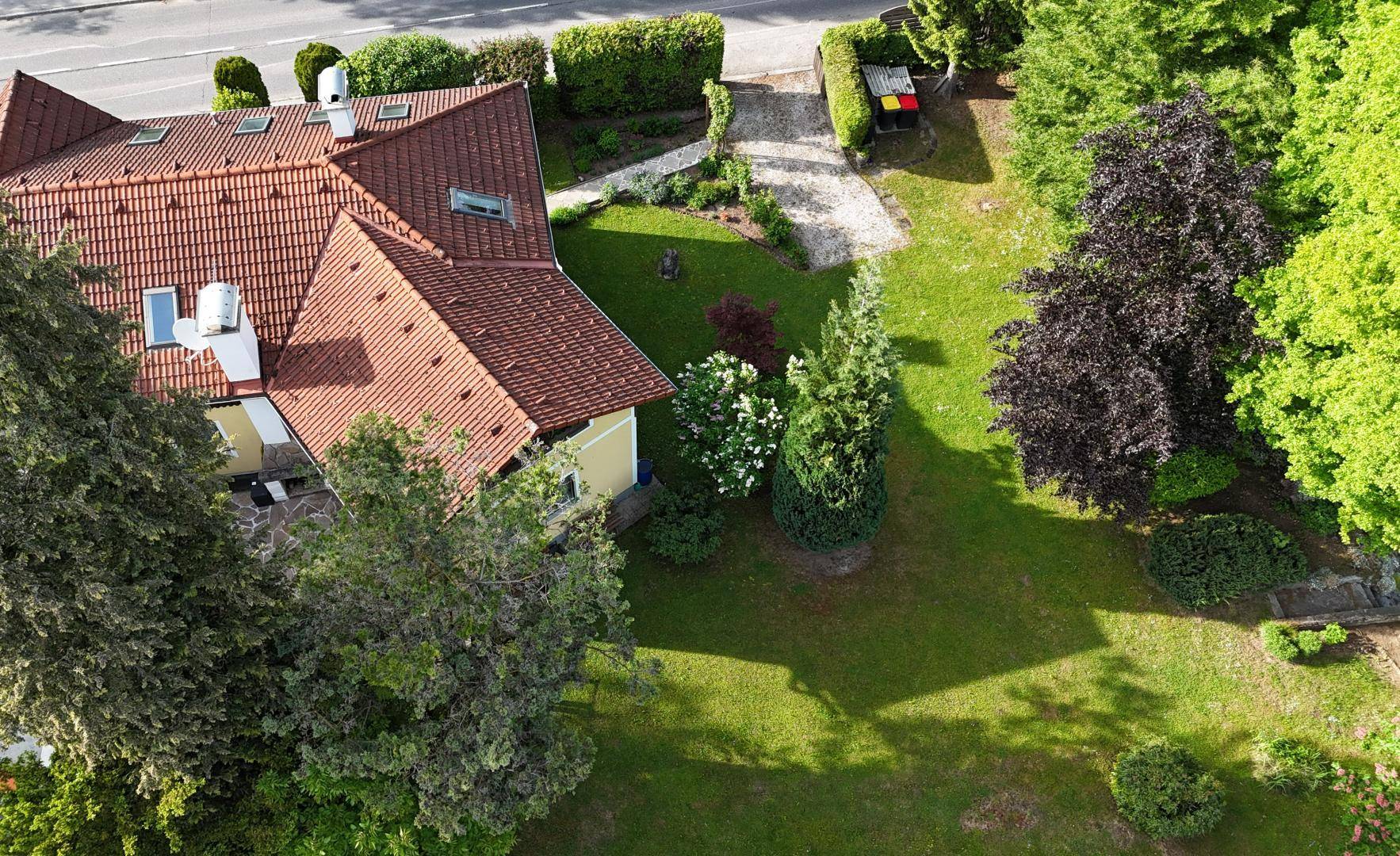 Luftaufnahme des Hauses mit großem Garten, umgeben von viel Grün und einer Straße.