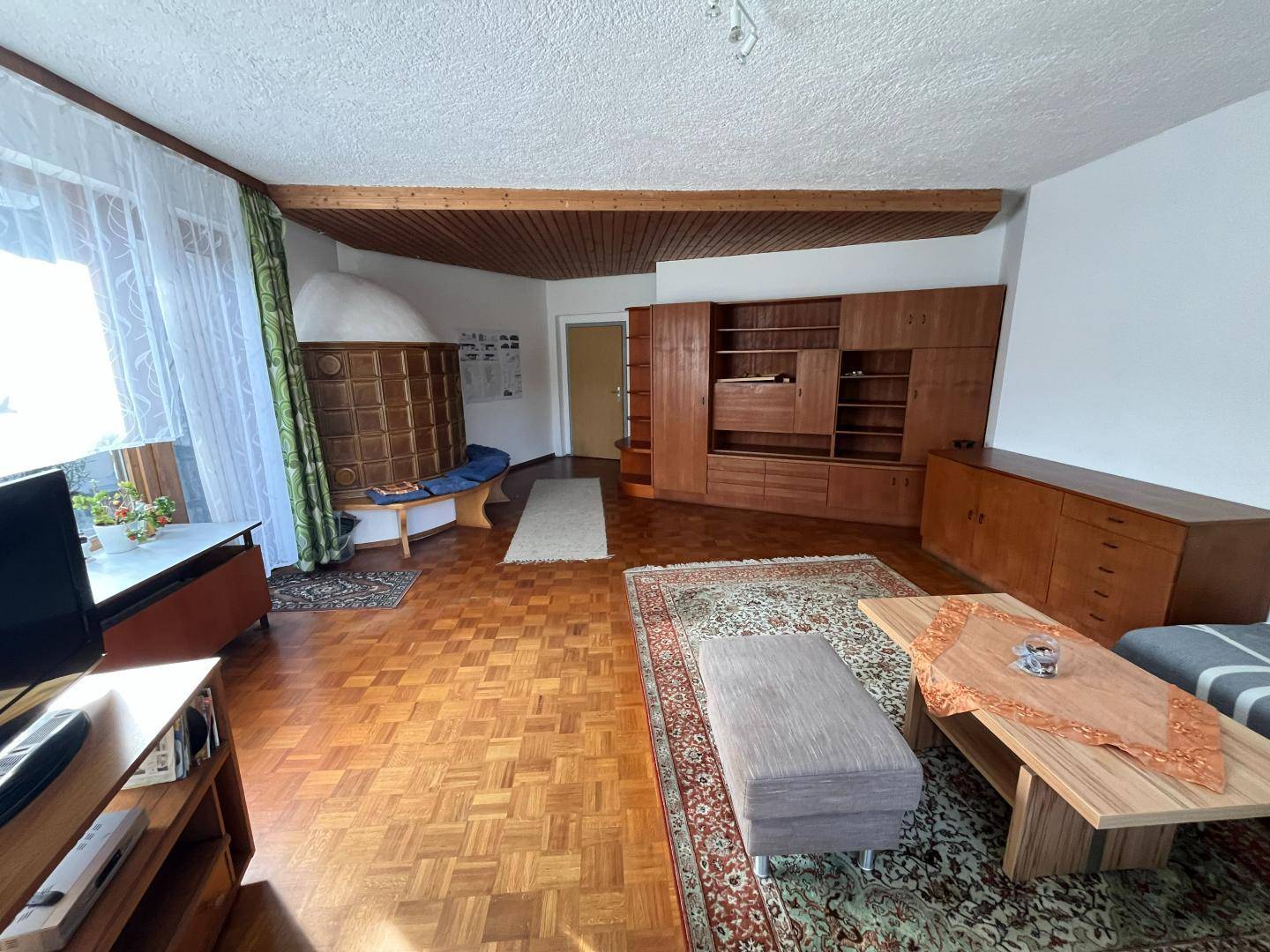 Gemütliches Wohnzimmer mit Kachelofen, Parkettboden und Holzmöbeln.