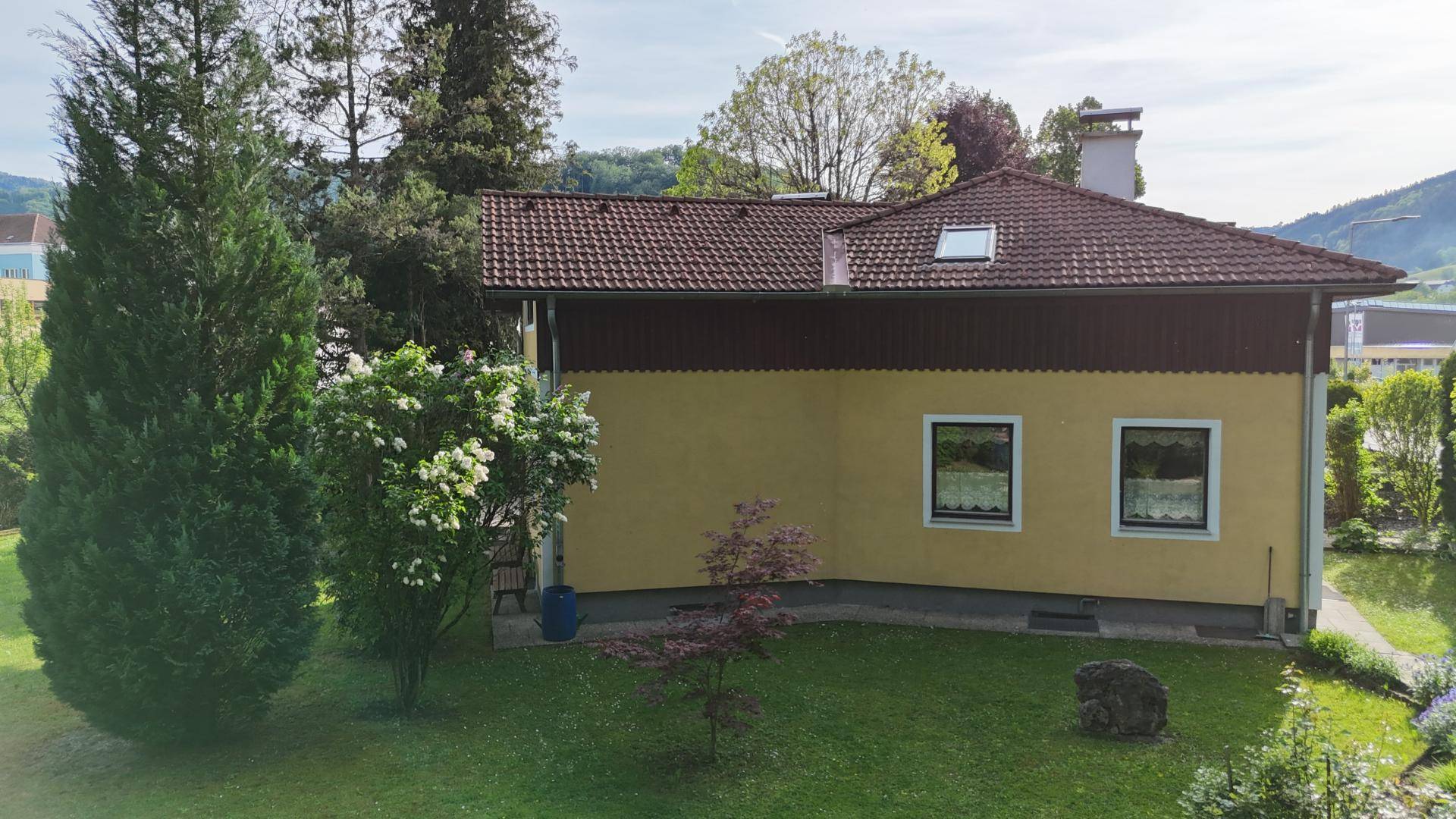 Seitenansicht des gelben Hauses mit brauner Holzverkleidung und einem grünen Garten.