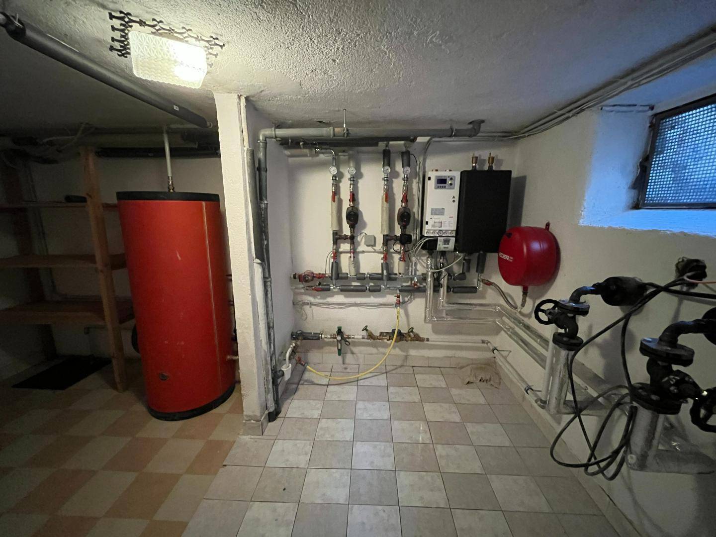 Heizungsraum im Keller mit Warmwasserspeicher und technischen Installationen.