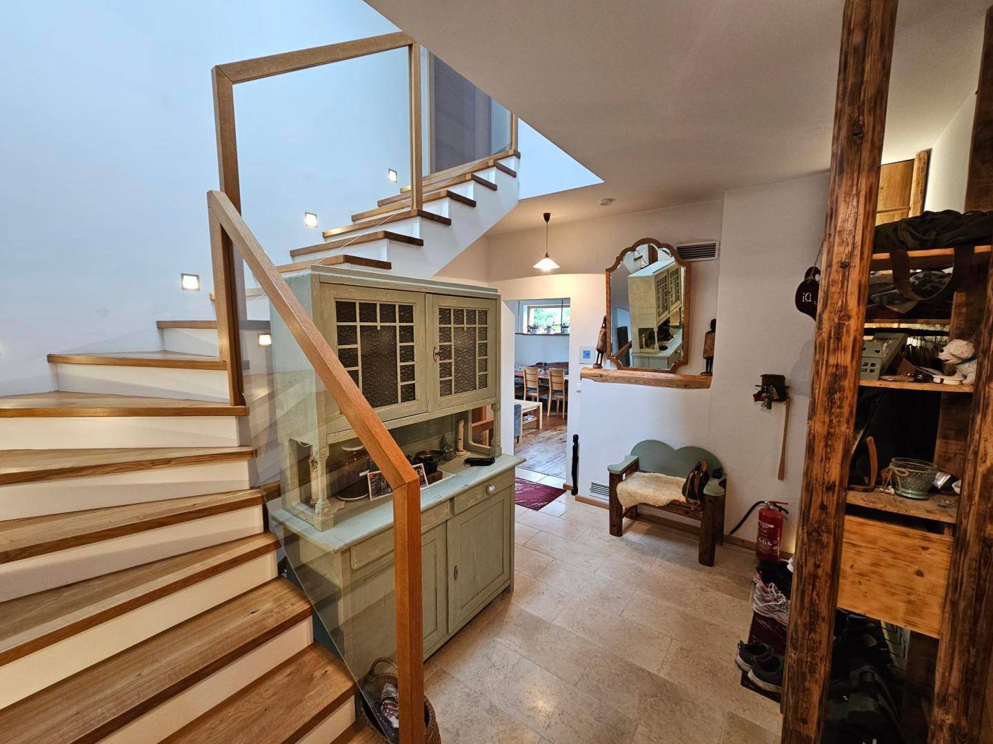 Heller Eingangsbereich mit Holztreppe, Glasgeländer und Natursteinboden.