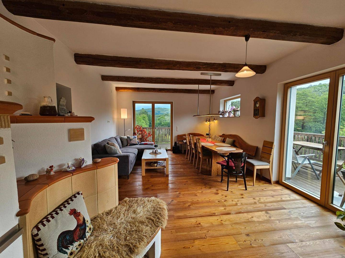 Gemütlicher Wohn-Essbereich mit Holzbalken, Kachelofen und Zugang zum Balkon.