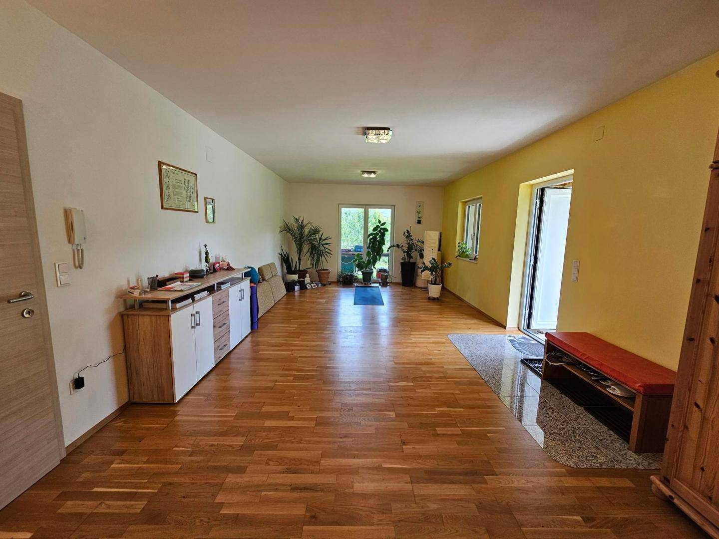 Geräumiger Mehrzweckraum mit Holzboden und Zugang zum Garten.