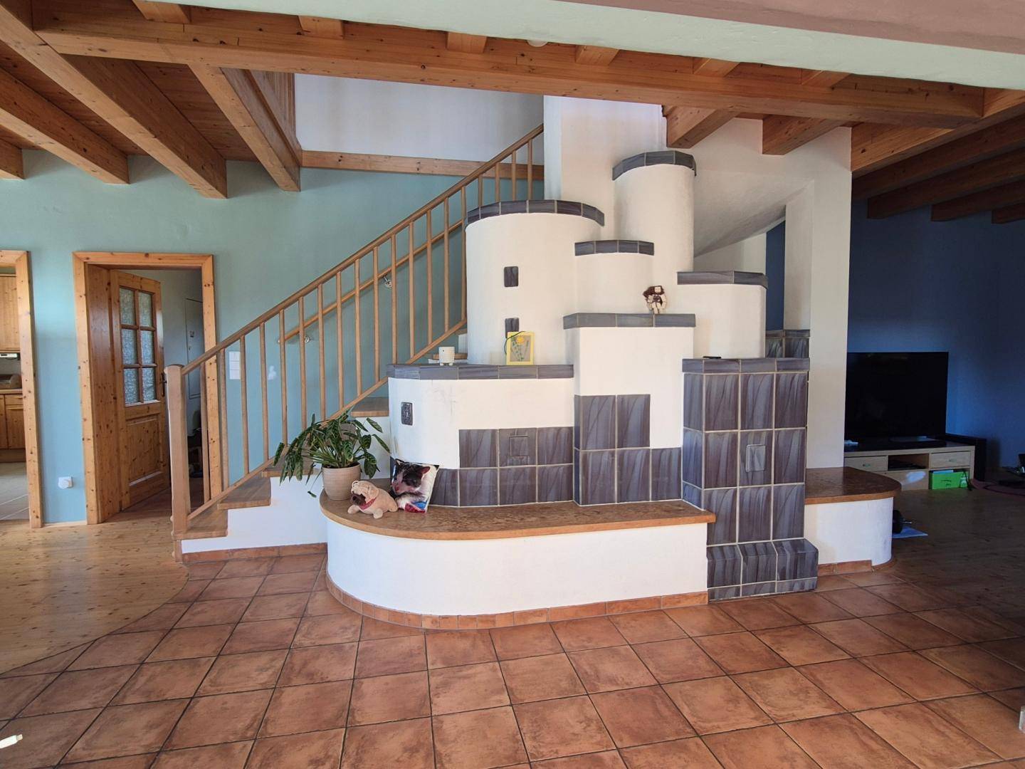 Gemütlicher Eingangsbereich mit traditionellem Kachelofen, Holztreppe und Fliesenboden.