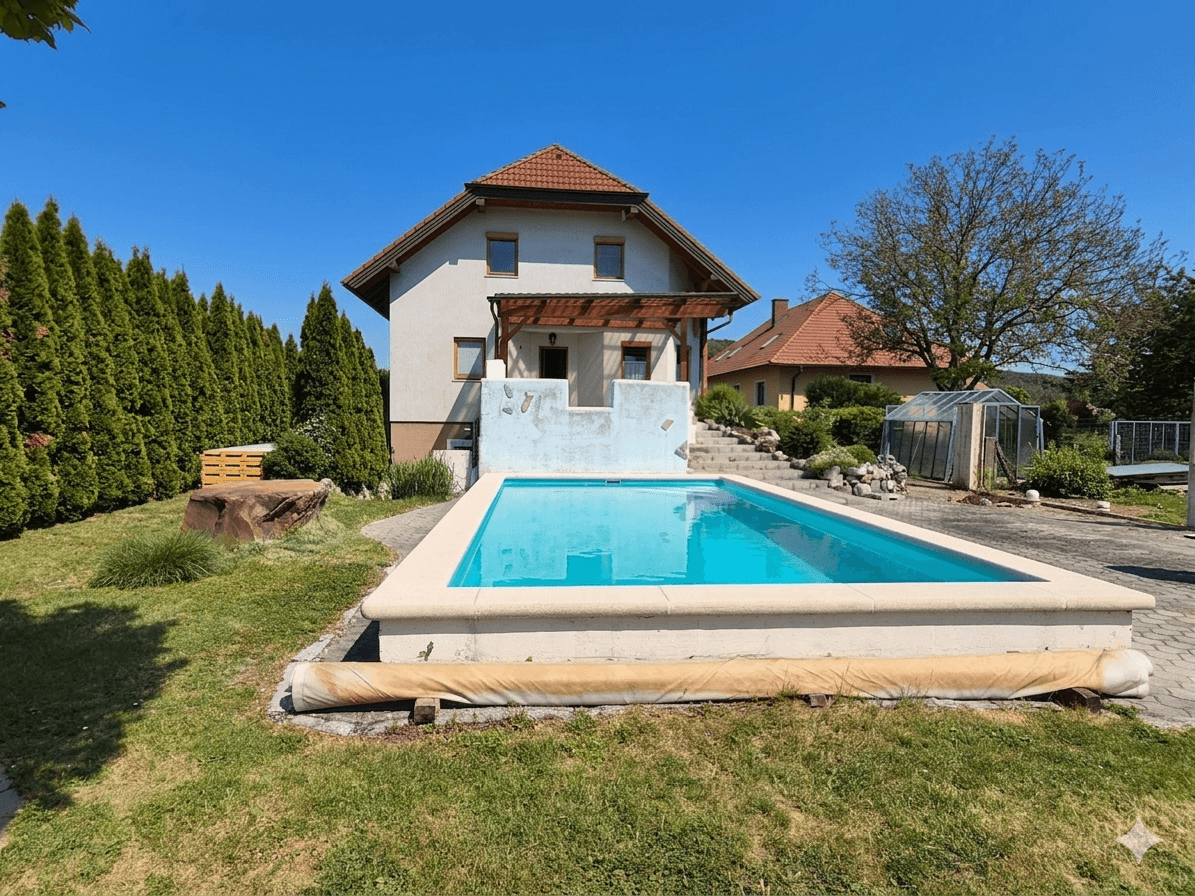 Einfamilienhaus mit privatem Swimmingpool und gepflegtem Gartenbereich unter blauem Himmel.
