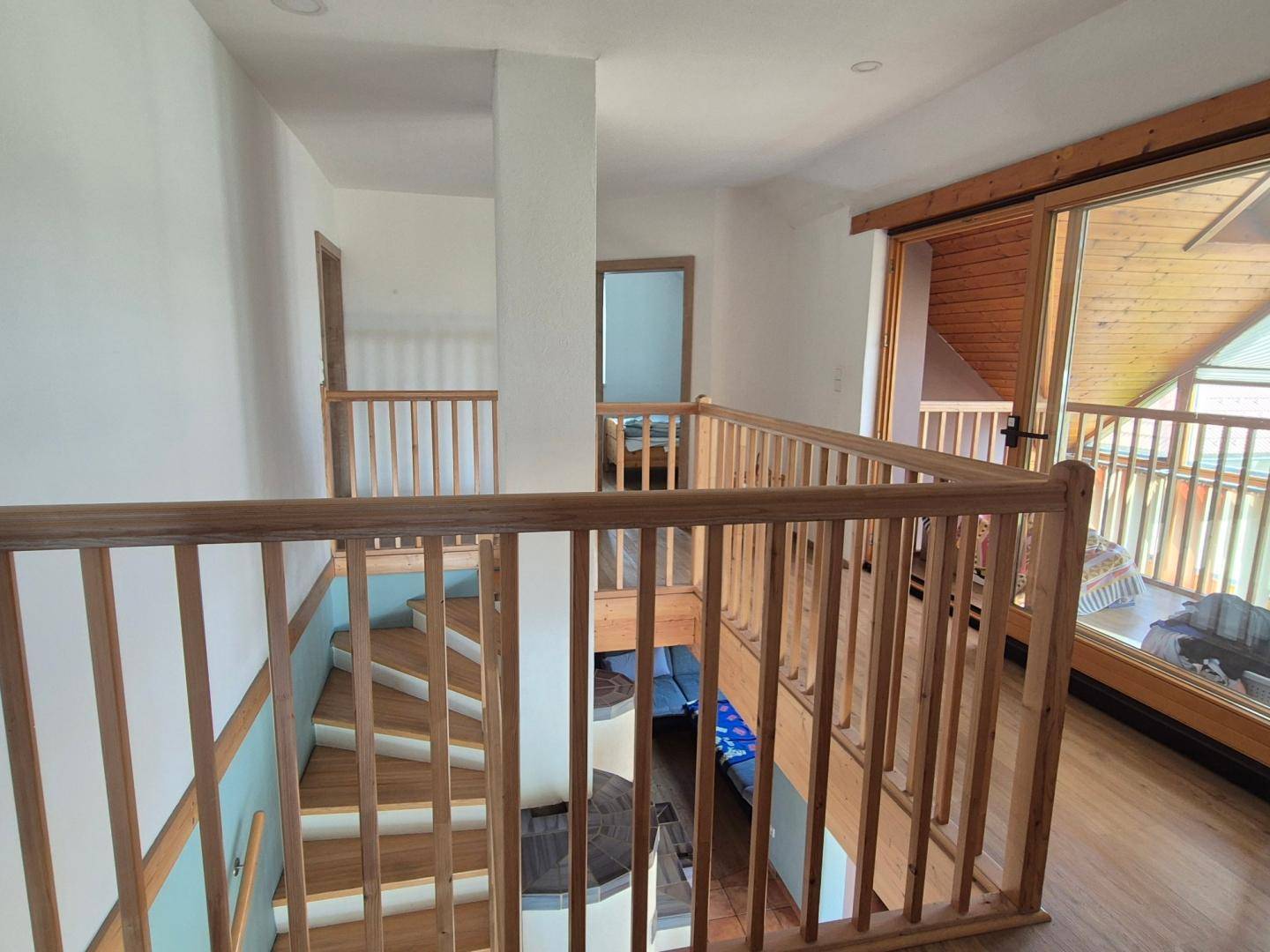 Heller Flur im Obergeschoss mit Holzgeländer und Zugang zu einem verglasten Balkon.