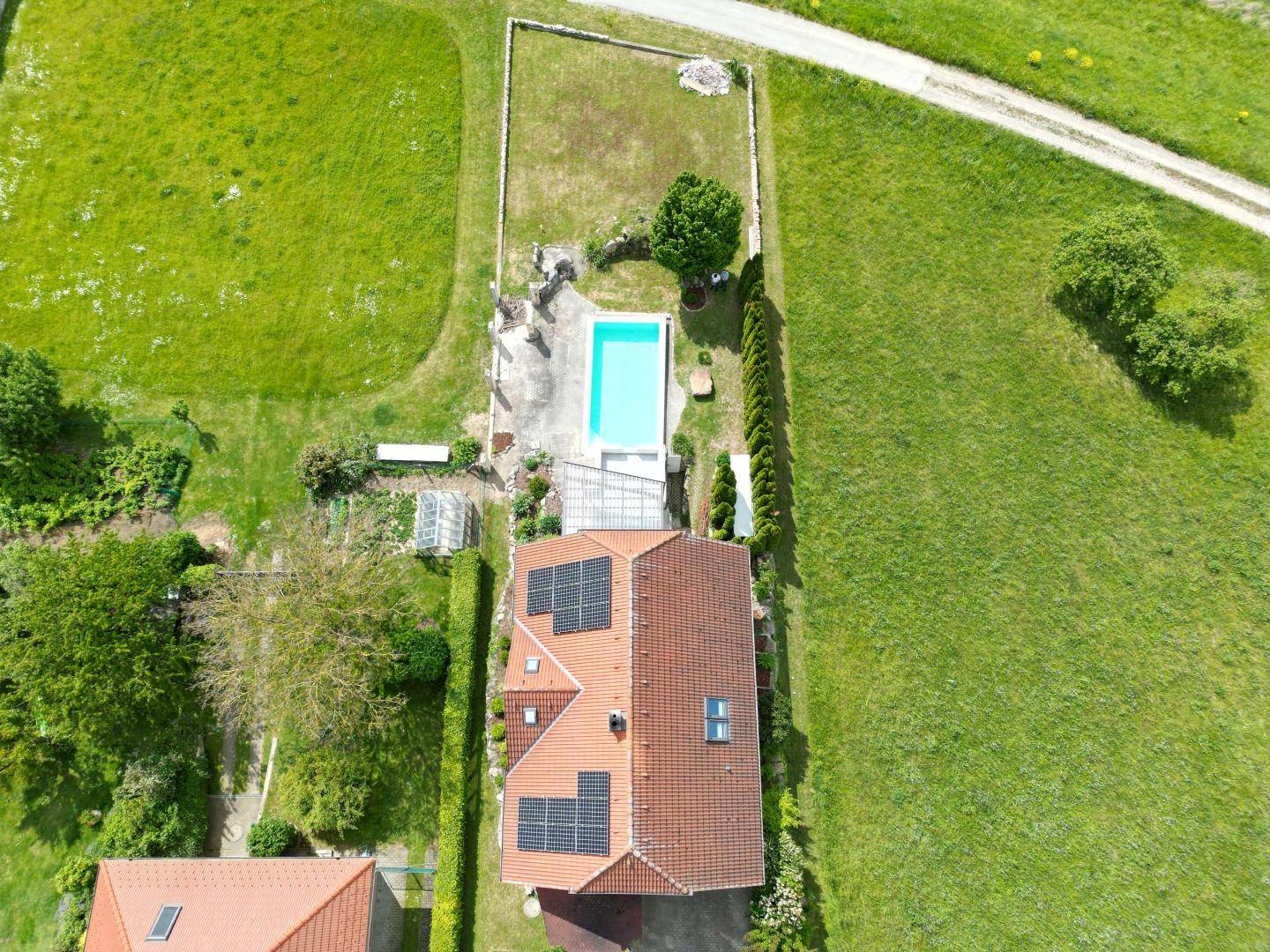 Draufsicht des Anwesens mit Haus, Pool und Gartenanlage, umgeben von Grünflächen.