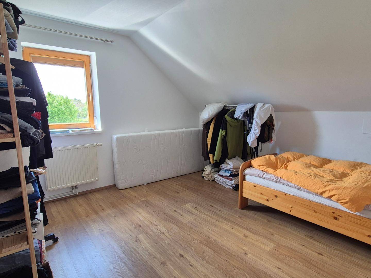 Schlafzimmer im Dachgeschoss mit Schrägen, Laminatboden und einem Fenster mit Ausblick.