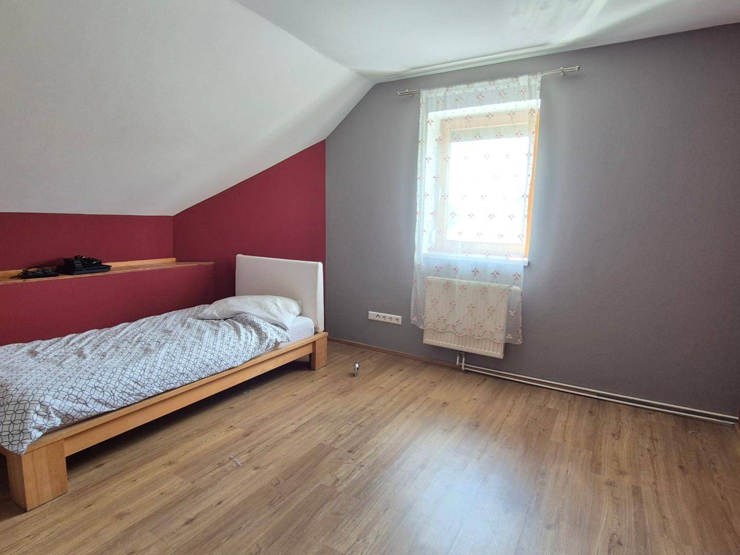 Dachgeschoss-Schlafzimmer mit farbigen Wänden, Laminatboden und einem Fenster.