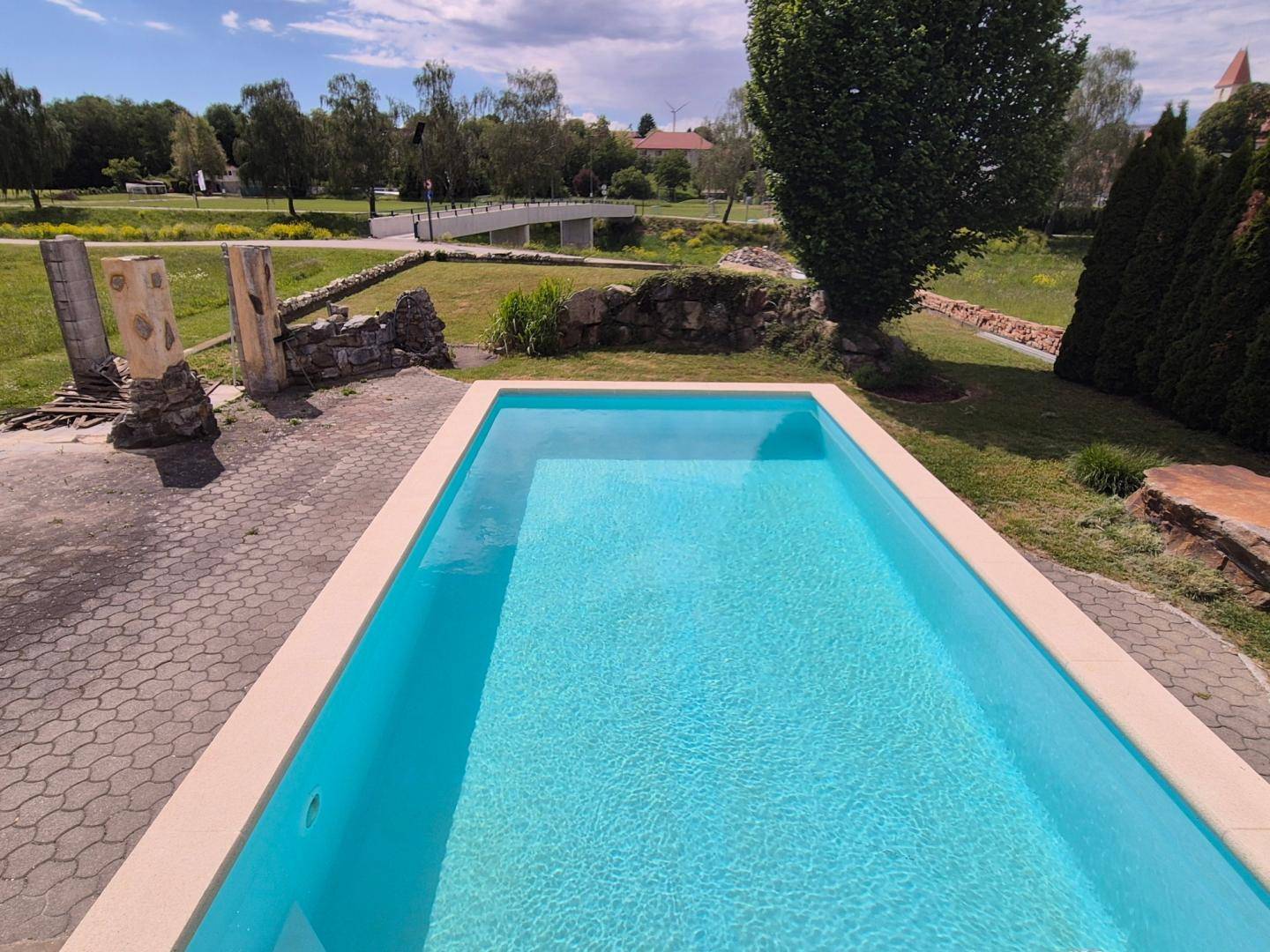 Klarer Swimmingpool mit gepflastertem Bereich und Blick auf die grüne Umgebung.