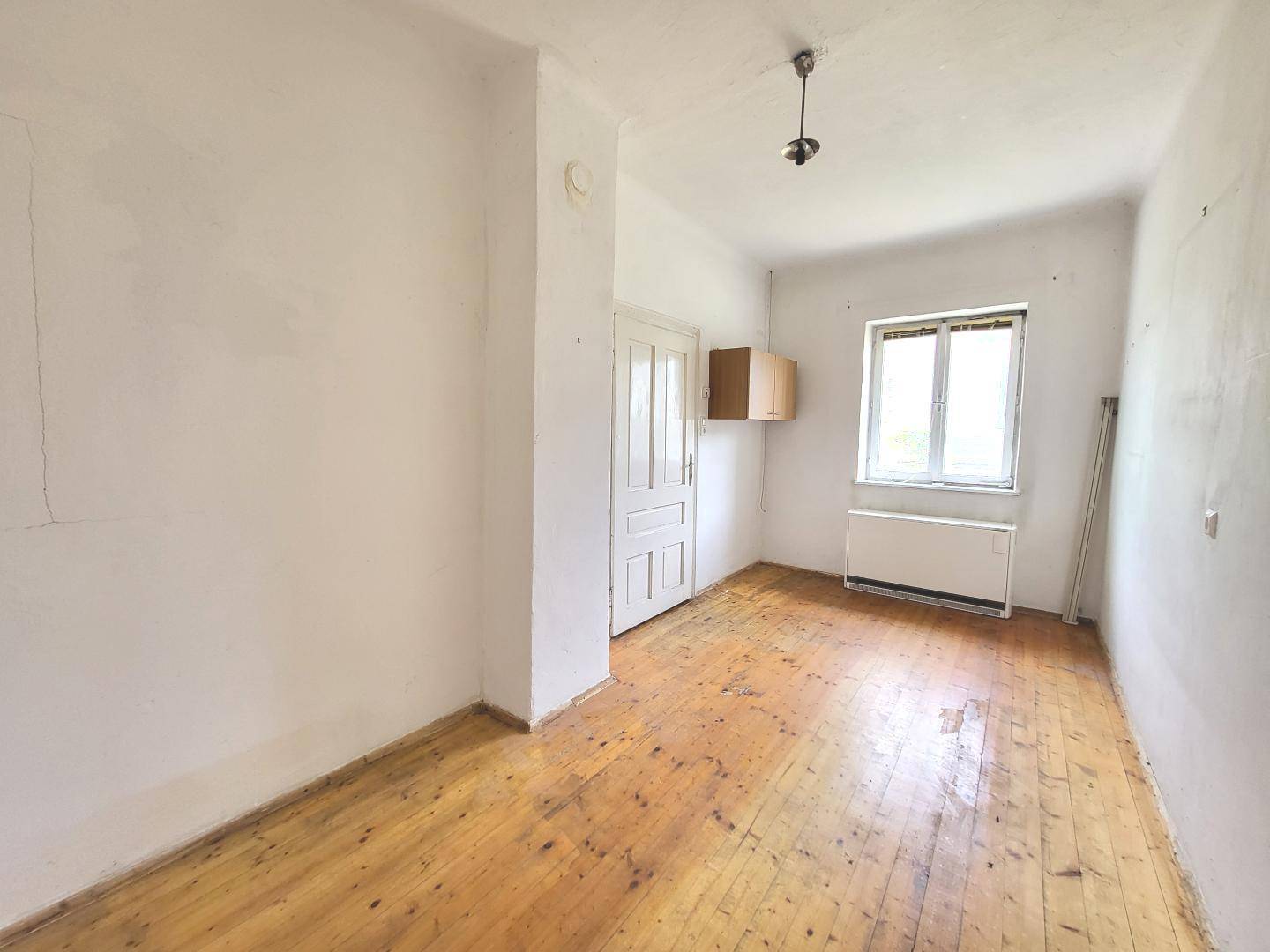 Leeres Zimmer mit hellen Wänden, Holzdielenboden und einem Fenster, das Tageslicht hereinlässt.