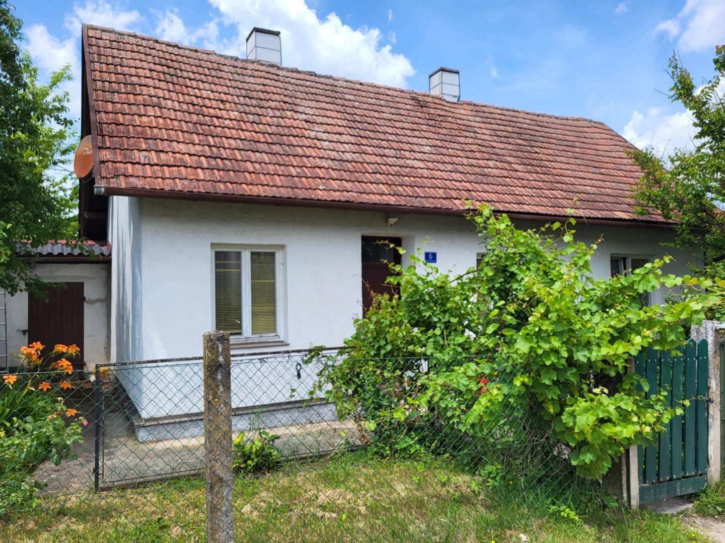 Ansicht eines traditionellen Hauses mit Ziegeldach, weißer Fassade und einem kleinen Schuppen im Hintergrund.
