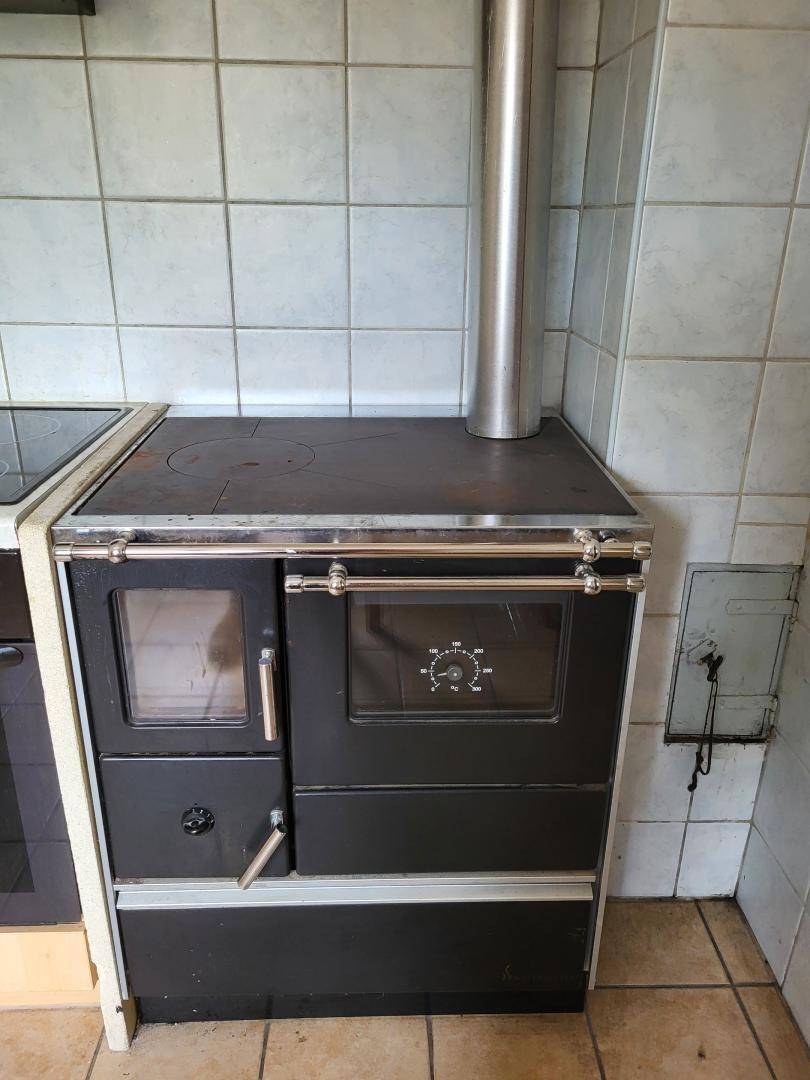 Detailansicht eines traditionellen Holzofens mit Kochfeld und Backofen in einer gefliesten Küche.