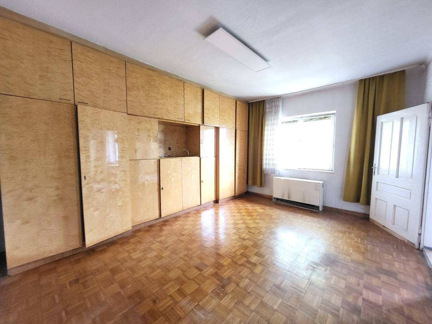 Geräumiges Schlafzimmer mit Einbauschränken, Parkettboden und einem Fenster mit Vorhängen.